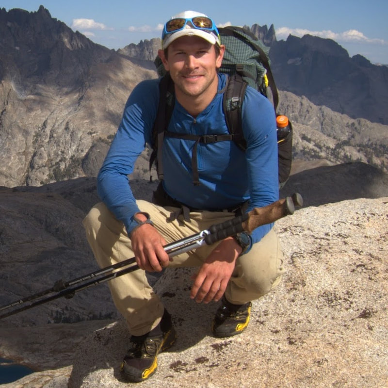 Man in blue shirt and beige pants with backpack on a mountain.