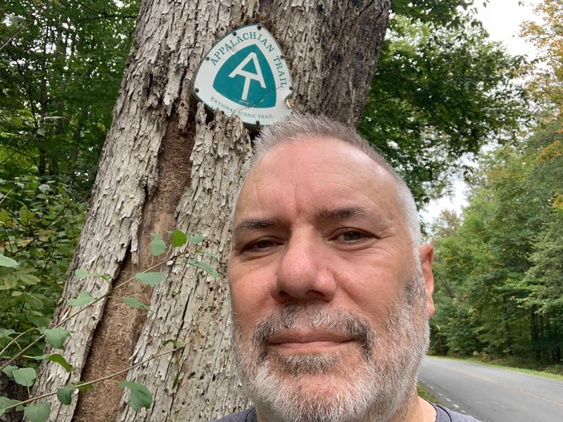 Man standing in front of a tree with green and white Appalachian Trail sign.