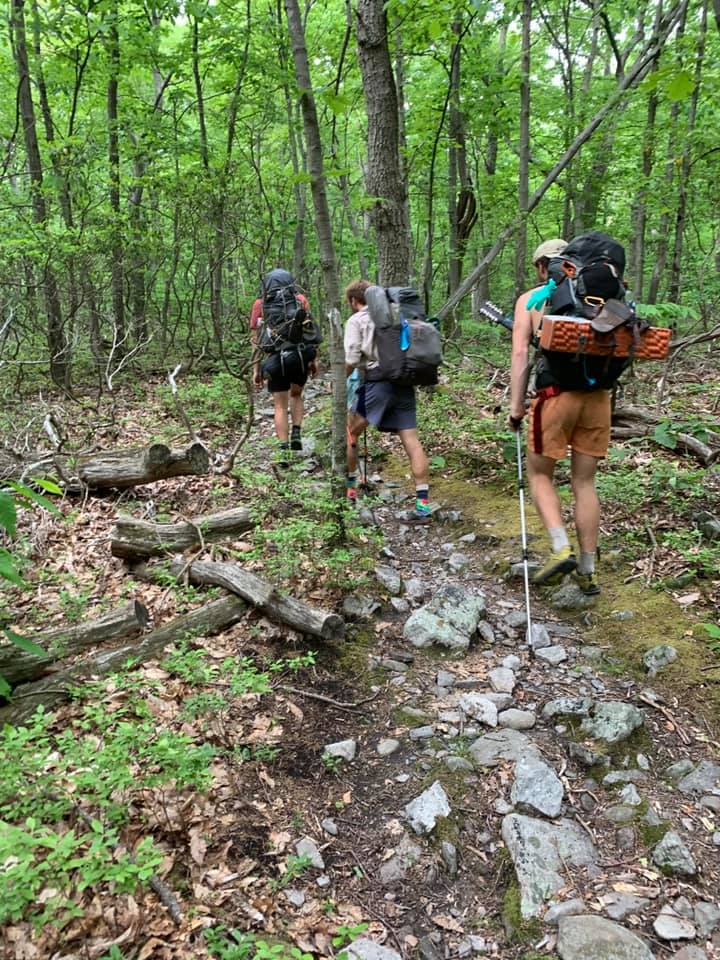 Three men with backpacks walking down a trail.