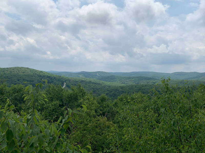 View from a trail of green hills, mountains, and cloudy sky.