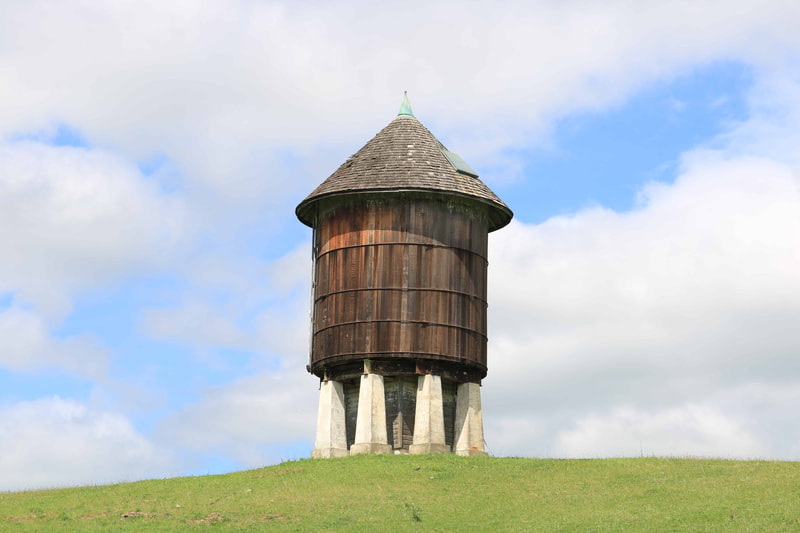Water tower on top of a green hill with cloudy sky in the background.