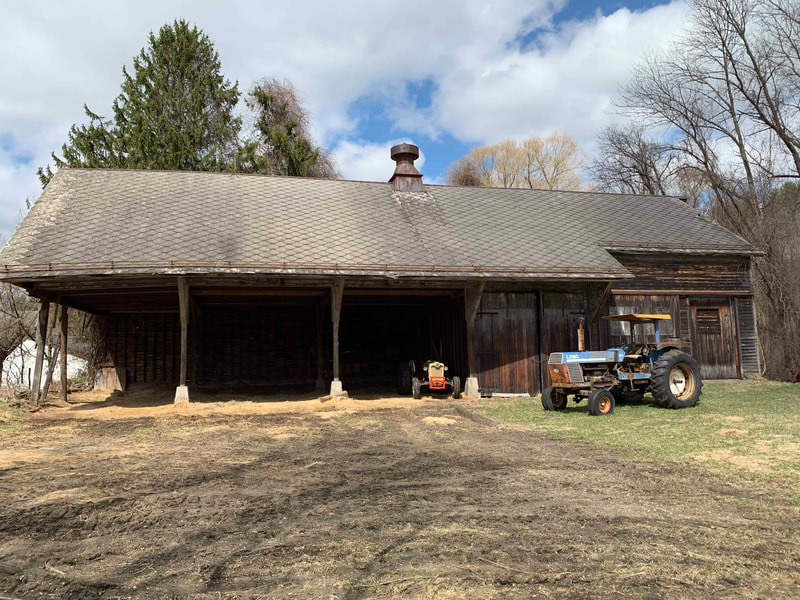 Dark brown wooden barn and tractor with cloudy blue sky in the background.