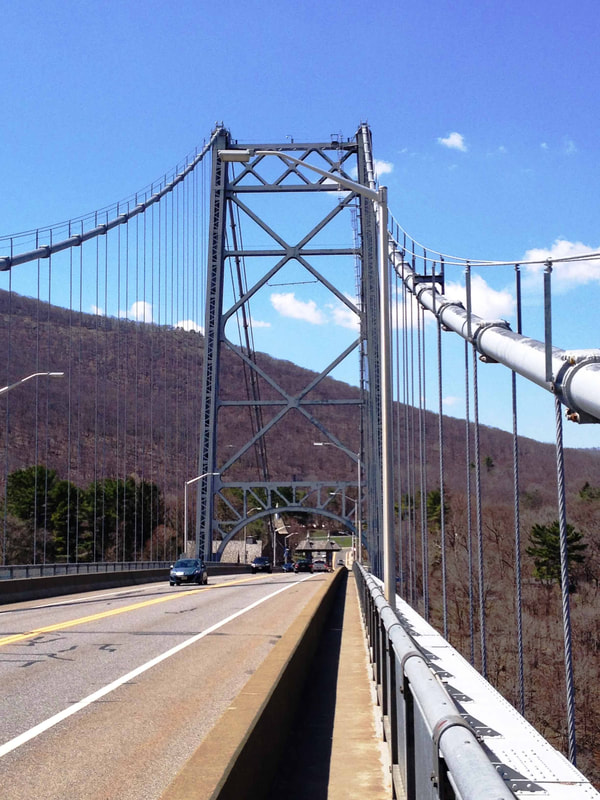 Suspension bridge with mountains and cloudy blue sky in the background.