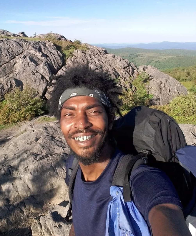 Man smiling with rocky terrain and trees in the background.