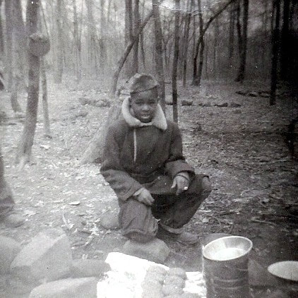 Young boy in winter coat and hat camping in woods.