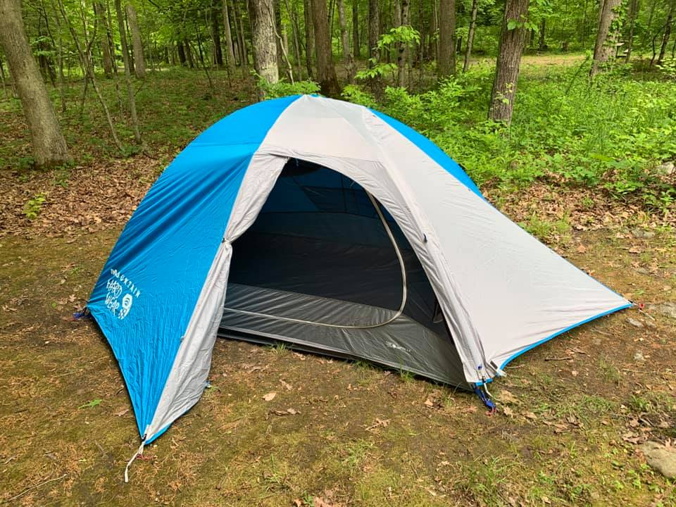 Blue and gray tent in a campground with trees and green groundcover in the background.